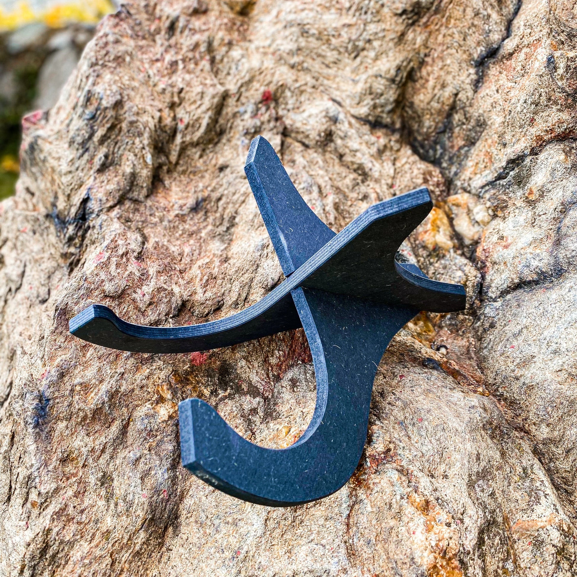 Einsatzbereiter schwarzer Ukulele Ständer aus Holz auf steiniger Fläche